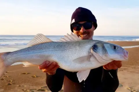 Glücklicher Angler präsentiert stolz seinen Fang: ein schöner Wolfsbarsch, gefangen mit einer speziellen Montage beim Wolfsbarsch angeln.