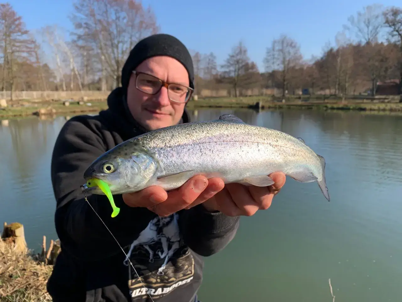 Glücklicher Angler hält eine frisch gefangene quellental forelle mit einem leuchtend grünen Köder im Maul.