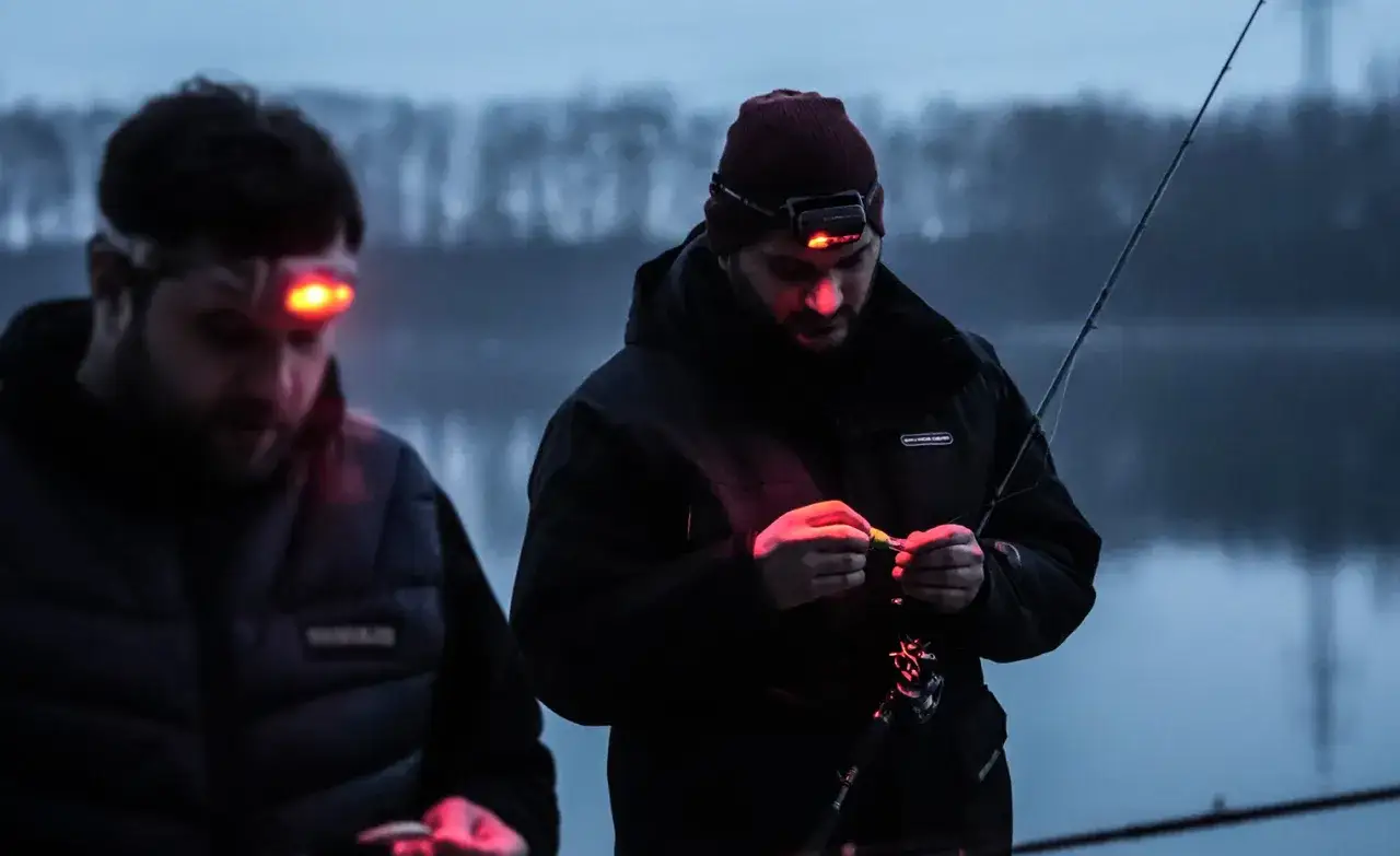 Zwei Angler bereiten sich auf das Nachtangeln vor. Mit Stirnlampen beleuchten sie ihre Köder und die Angelruten im Dämmerlicht.