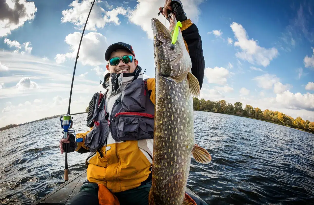Gl&uuml;cklicher Angler pr&auml;sentiert stolz seinen Fang beim Bodden-Angeln vom Ufer. Ein gro&szlig;er Hecht h&auml;ngt an der Angelrute.