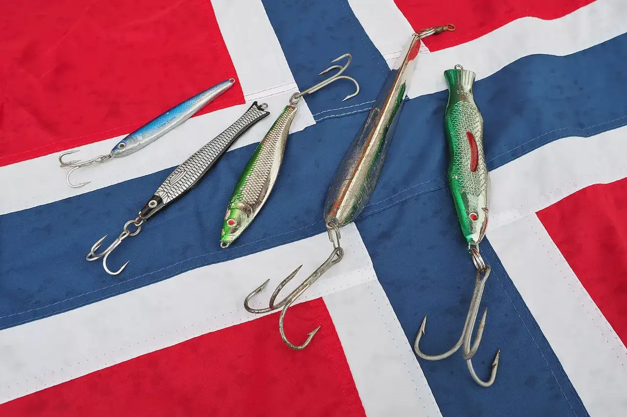 Fünf Pilker und Haken liegen auf einer norwegischen Flagge. Bereit für das Pilken vom Ufer.