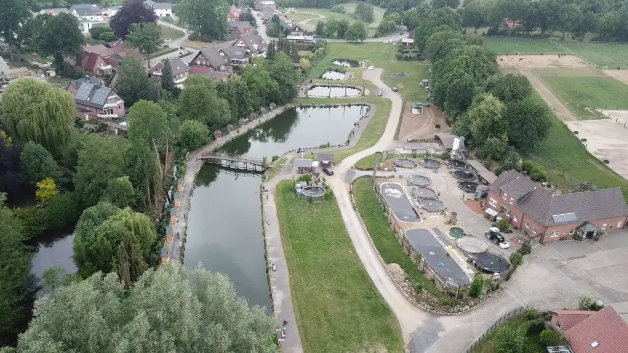 Luftaufnahme einer Anlage mit Teichen, die f&uuml;r quellental forellen genutzt werden. Mehrere runde Becken und ein langer Teich sind zu sehen.